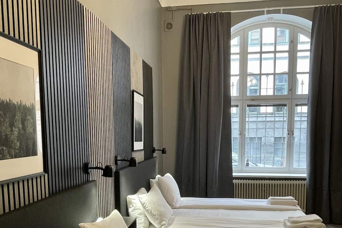 Ein Hotelzimmer mit zwei Betten, einem großen Fenster mit Vorhängen, einem Wandbild und einer Deckenleuchte.