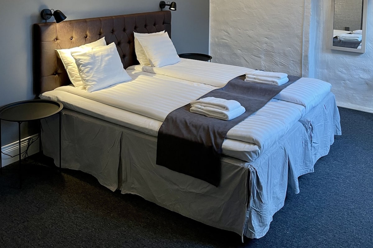 A neatly made double bed with a headboard, a bedside table, and a wall-mounted telephone.