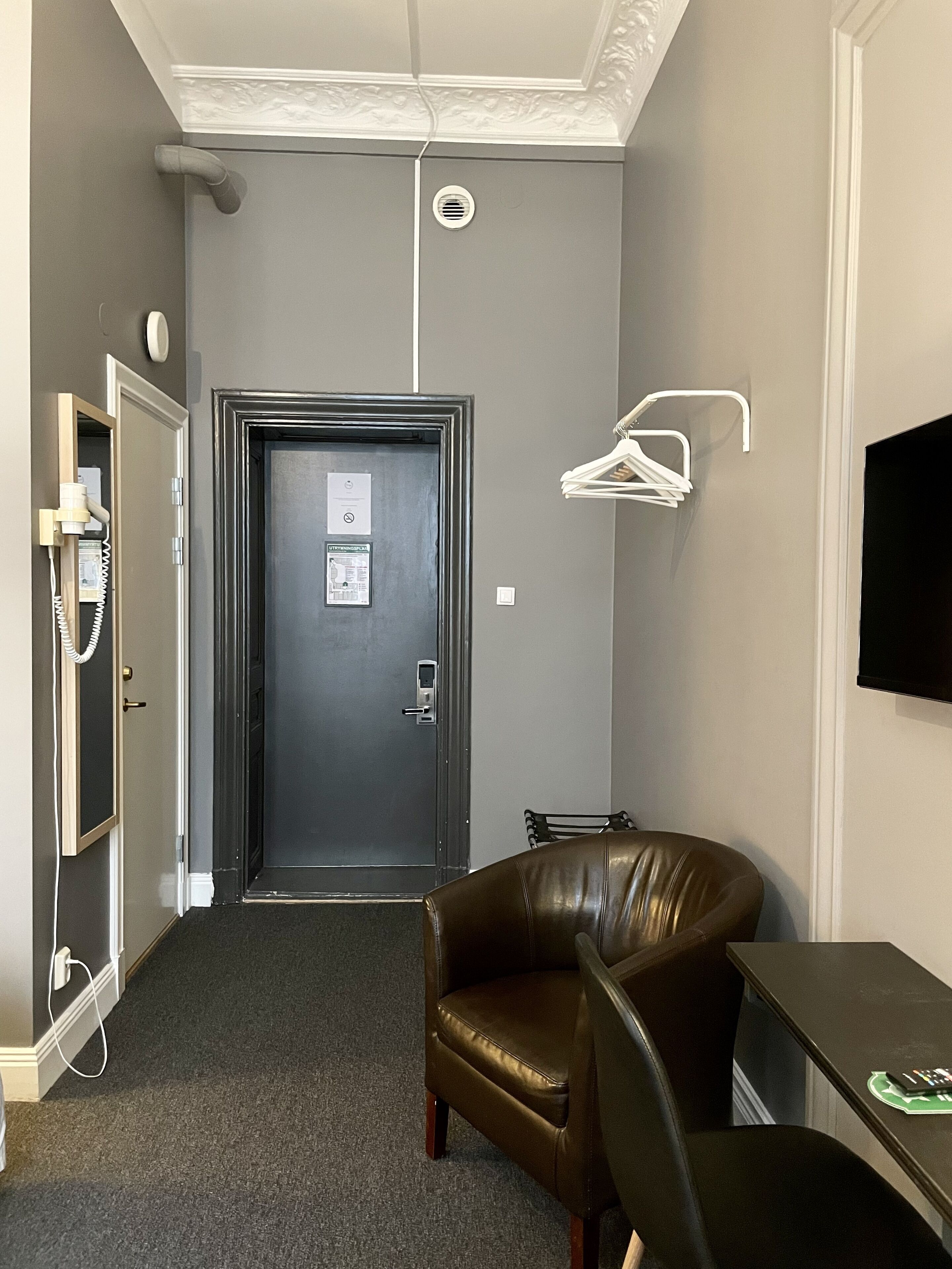 A narrow hallway with a door, a coat rack, a chair, and a table.