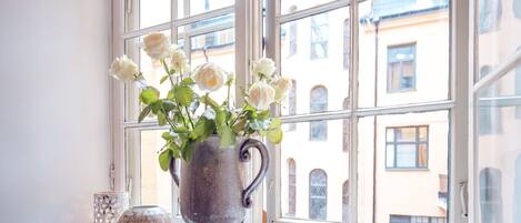 Una ventana con vistas a edificios, un jarrón con flores blancas y dos jarrones decorativos en el alféizar.