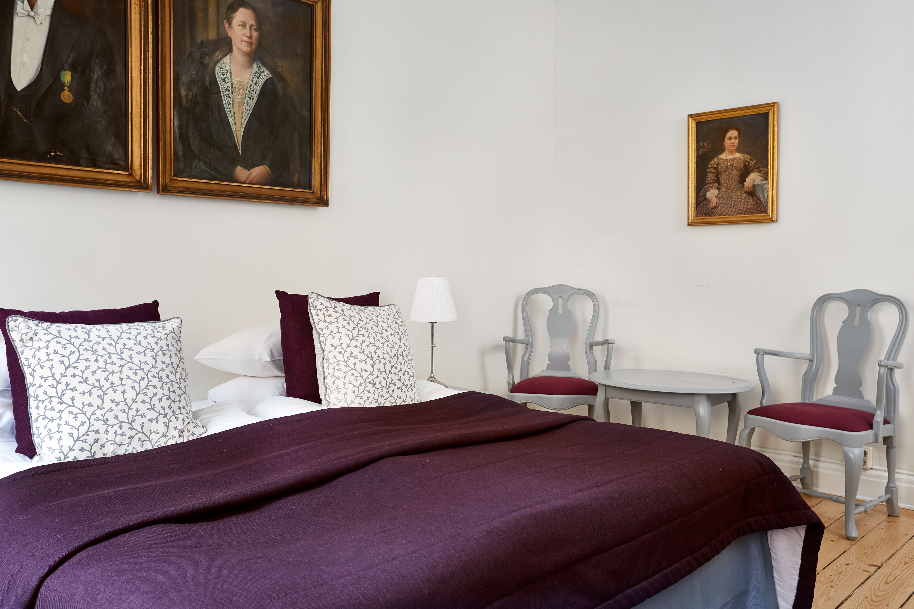 Una habitación de hotel con una cama grande, dos sillones, una mesita y dos cuadros en la pared.