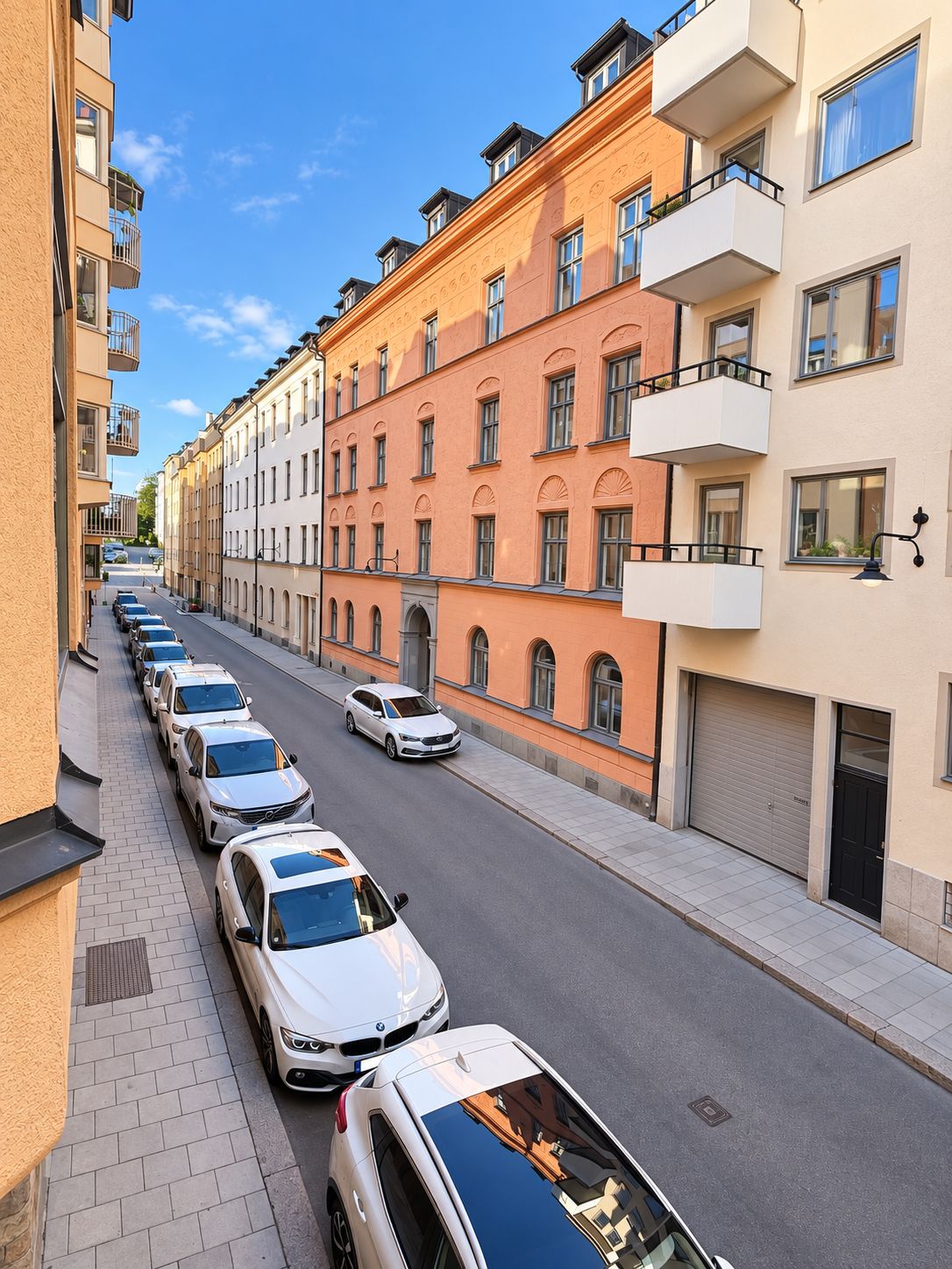 A row of parked cars along a street lined with multi-story buildings.