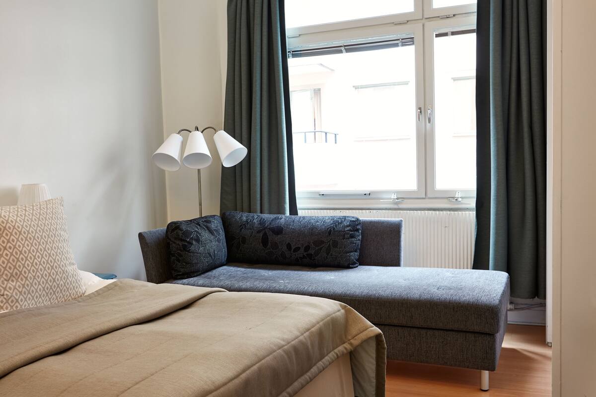 Una camera da letto con un letto, un divano grigio e una finestra con tende.