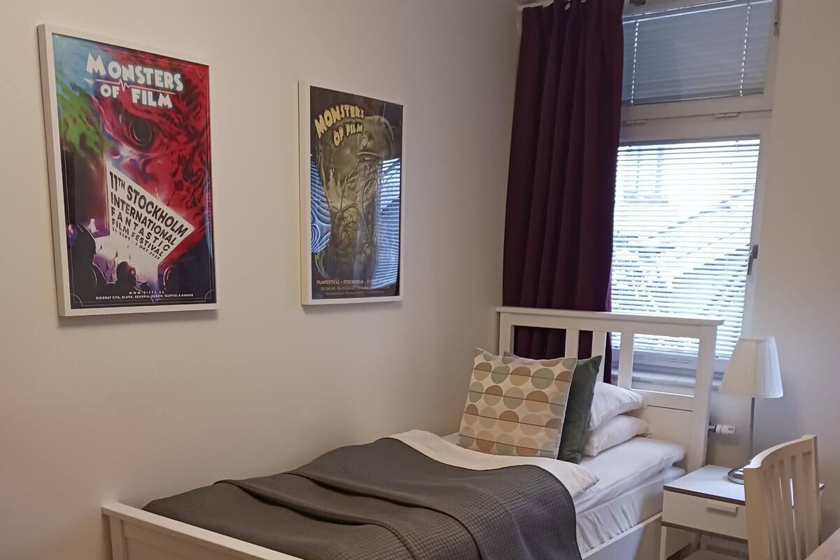 Una camera da letto con un letto, una scrivania, una sedia, una finestra con tende e due poster appesi al muro.