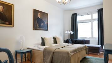 A bedroom with a bed, bedside tables, a desk, a chair, a window with curtains, and a painting on the wall.