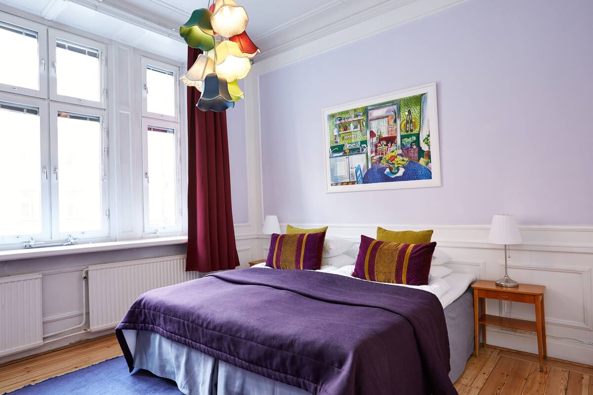 Una camera da letto con un letto grande, una finestra con tende, un quadro appeso al muro e un comodino con una lampada.