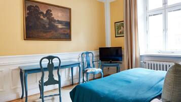 Una habitación con una cama, un escritorio, una silla, un televisor y un cuadro en la pared.