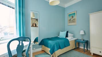Un dormitorio con cama, una silla, un escritorio, una lámpara y obras de arte en las paredes.