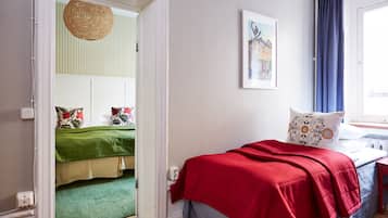 A bedroom with a bed, a window with curtains, a door leading to another room, and a wall with a framed picture.