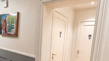 A hallway with a red carpet leading to a WC/shower area, white walls, and a framed picture on the left.