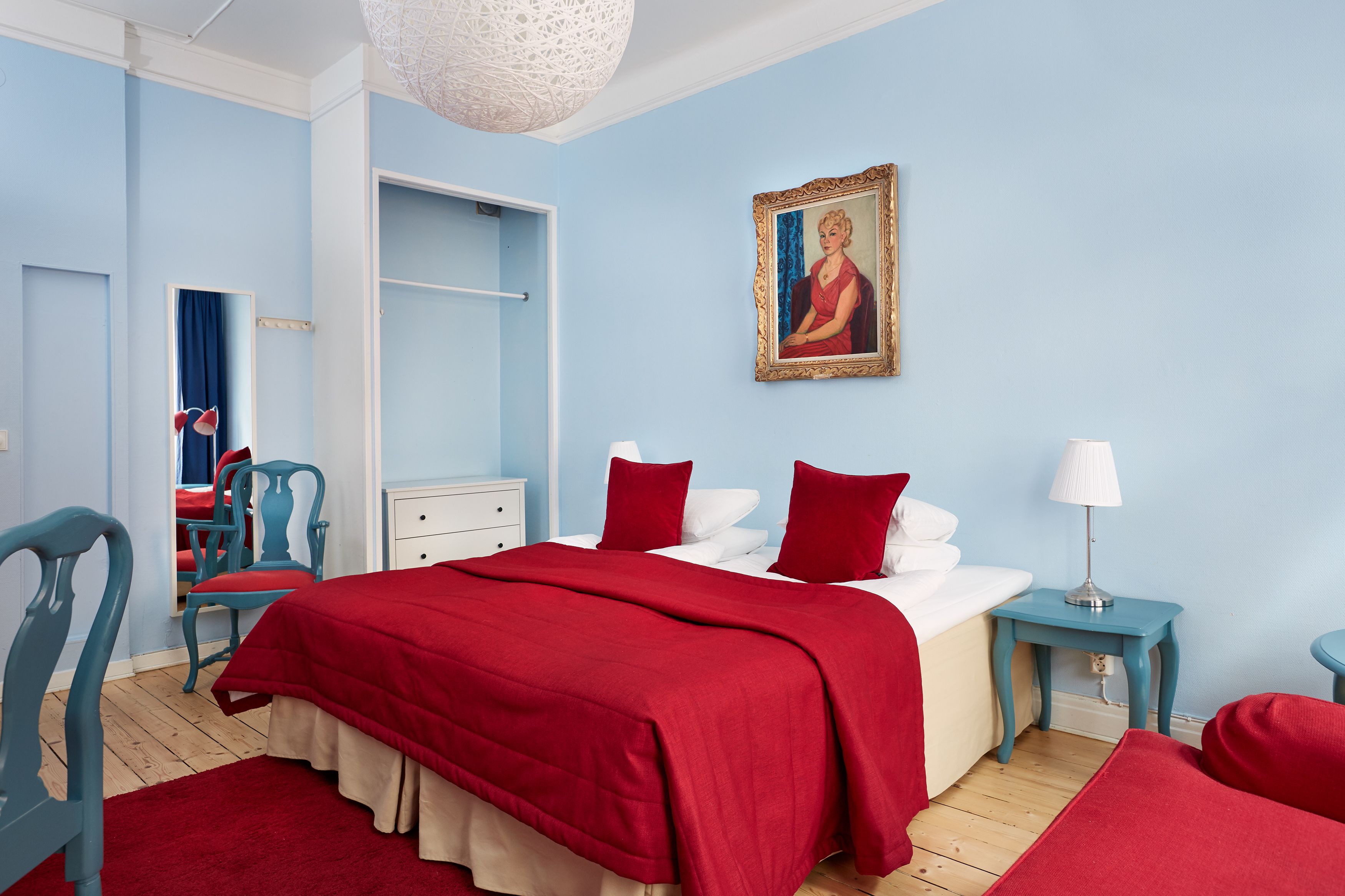 Un dormitorio con una cama, una silla, una mesita de noche, una lámpara y un cuadro en la pared.