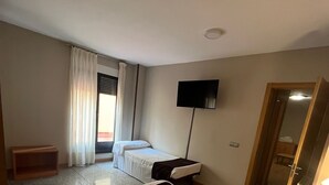 A hotel room with two beds, a TV, a wooden bench, and a door leading to a bathroom. - JCH Congreso (Salamanca)