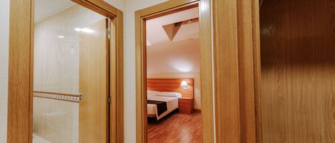 A hallway leading to a bedroom with wooden flooring, a bed, and a nightstand with a lamp.
