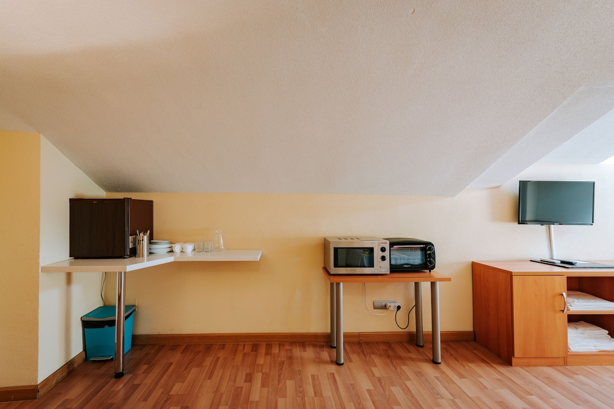 Uma pequena cozinha compacta com micro-ondas, uma mesa pequena, um armário e uma TV em um suporte.