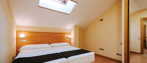 Habitación de hotel con tragaluz, cabecera de madera, dos lámparas de noche y una cama grande.