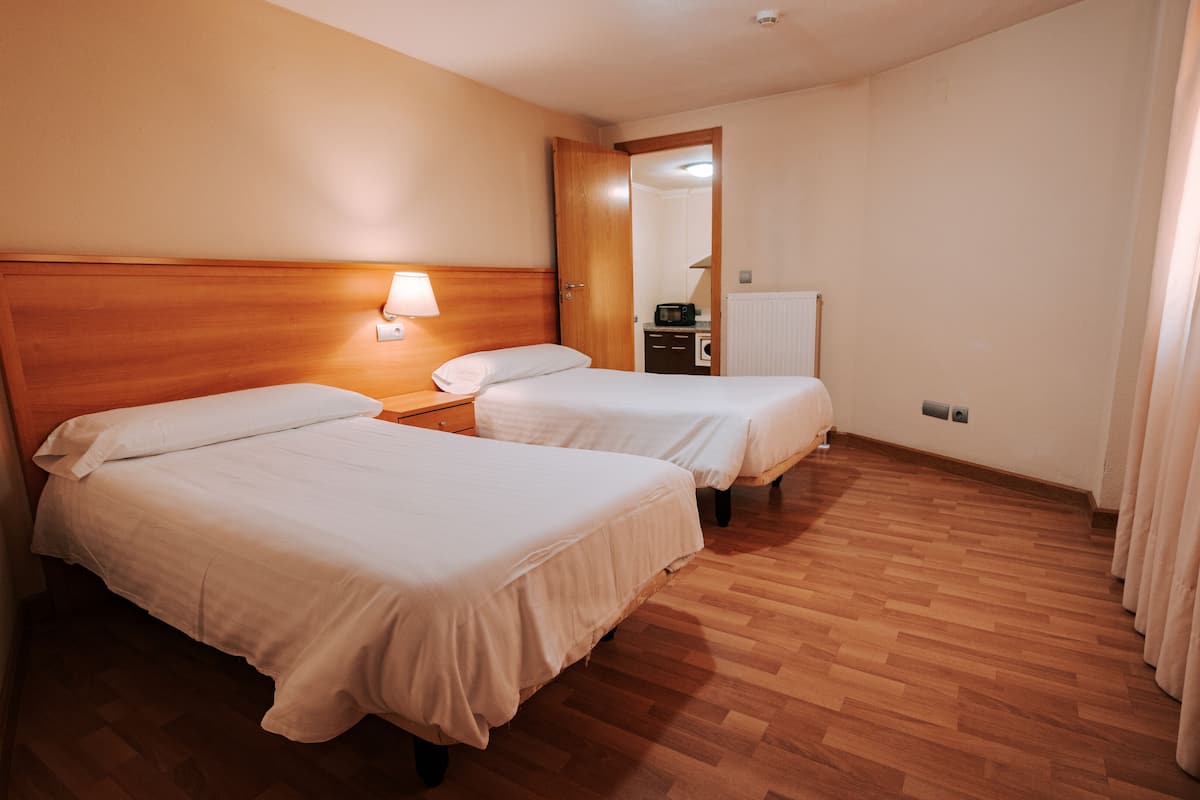 Quarto de hotel com duas camas, cabeceira de madeira, abajur, mesa pequena, micro-ondas e radiador.