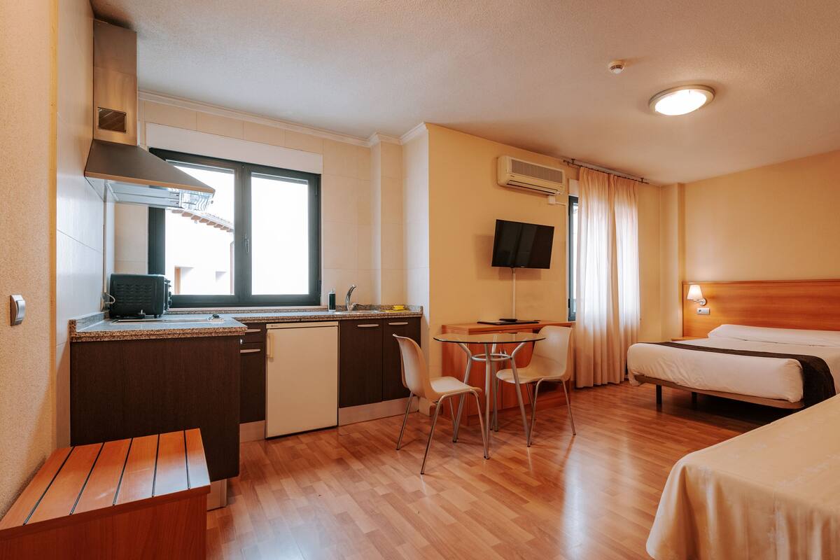 Quarto de hotel com cama, escrivaninha com computador, televisão e pequena mesa com cadeiras.