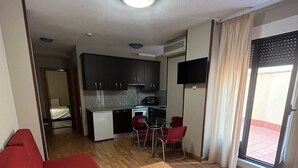 A compact living space with a kitchenette, a dining area, and a red sofa. - JCH Congreso (Salamanca)