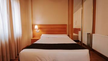 A hotel room with a bed, a nightstand with a lamp, a mirror, and a radiator.