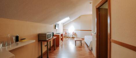 A compact hotel room with a kitchenette, a dining area, and a bed.
