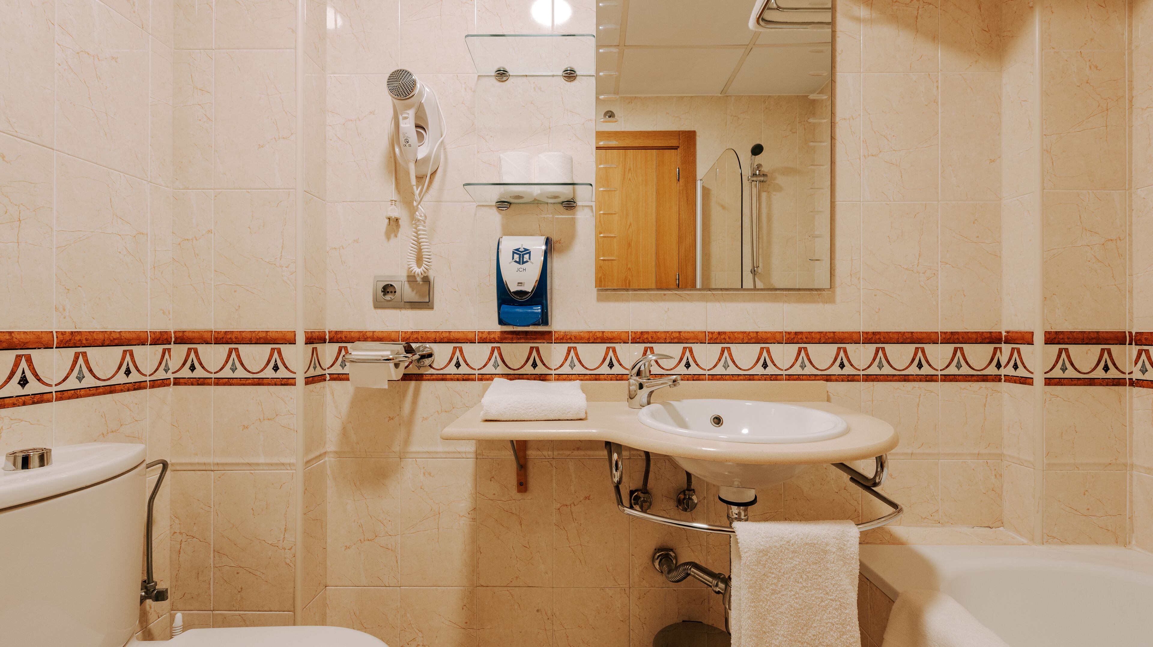 A bathroom with a toilet, sink, and shower. There is a towel rack, a soap dispenser, and a mirror.