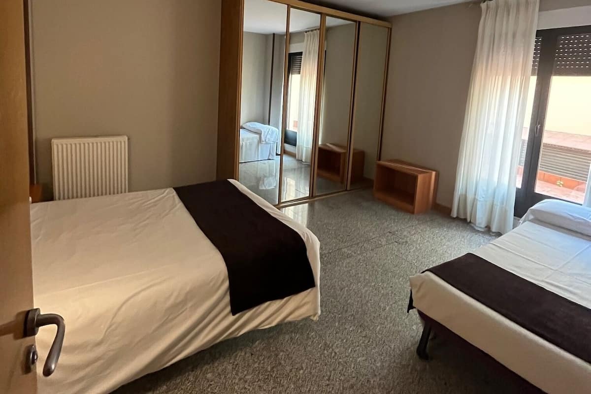 Quarto de hotel com duas camas, um espelho, um radiador e vista para o exterior.