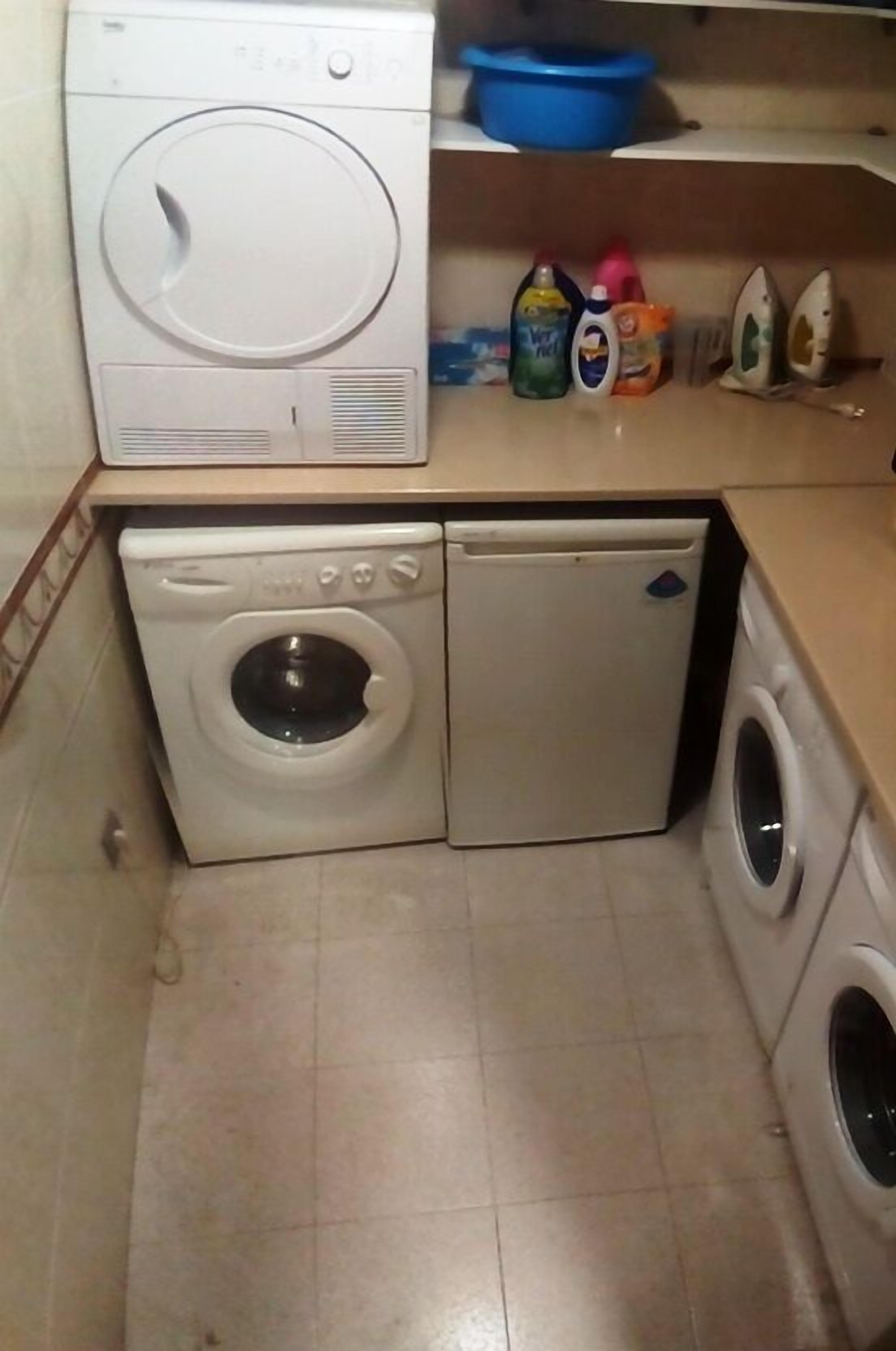 Un área de lavandería compacta con lavadora y secadora de carga frontal, un estante con productos de limpieza y un lavabo azul sobre la encimera.