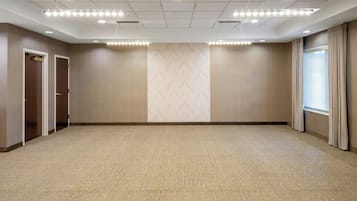 A large, empty conference room with a carpeted floor, wooden panel walls, and a large window with curtains.