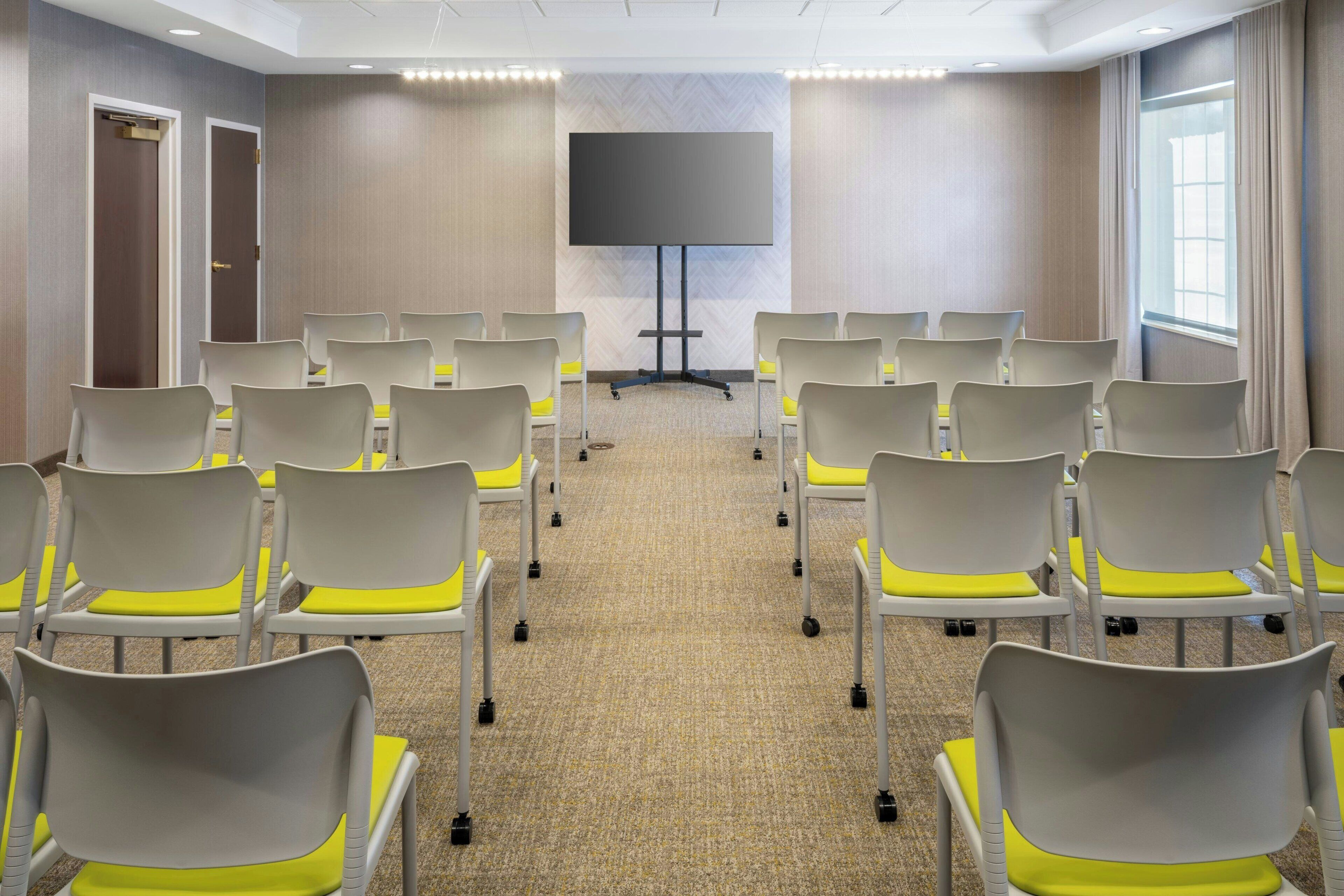 A conference room with rows of chairs, a large screen, and a carpeted floor.