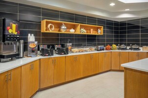 A modern kitchen with a coffee station, a fruit display, and a variety of breakfast items.