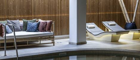 A modern spa area with a wooden wall, a cushioned seating area, and a massage table.