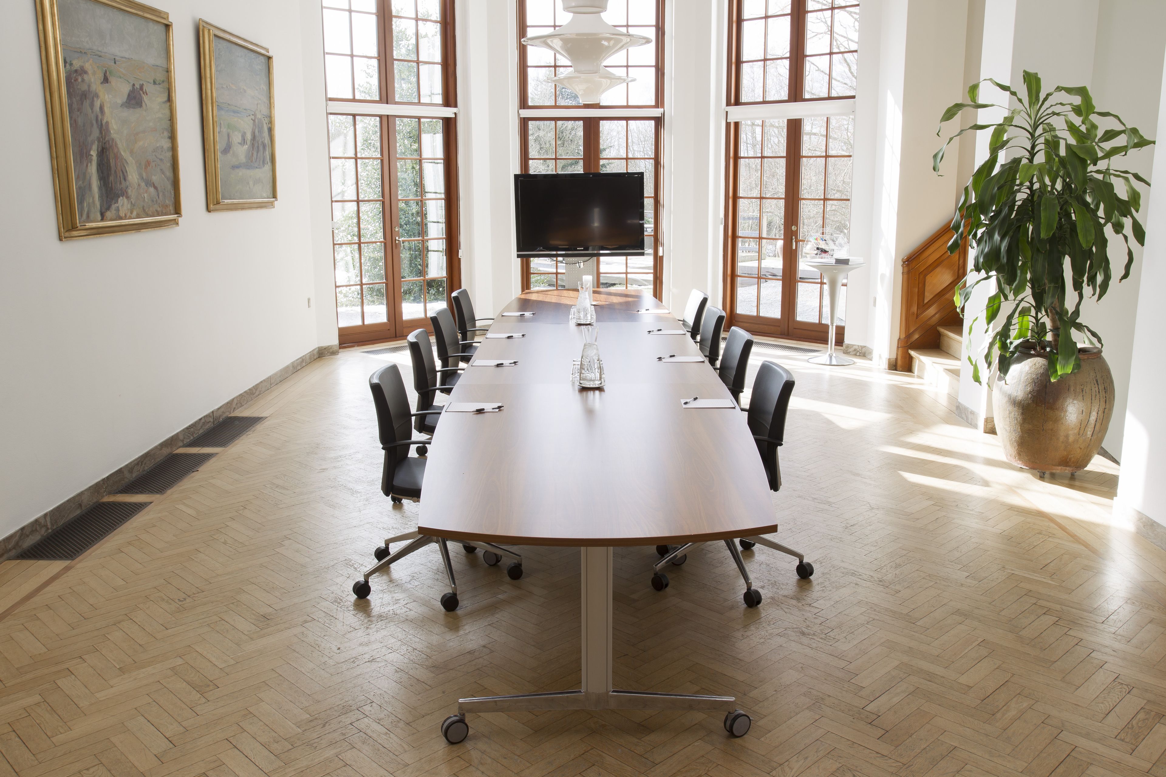 A conference room with a large table, chairs, a TV, and artwork on the walls.