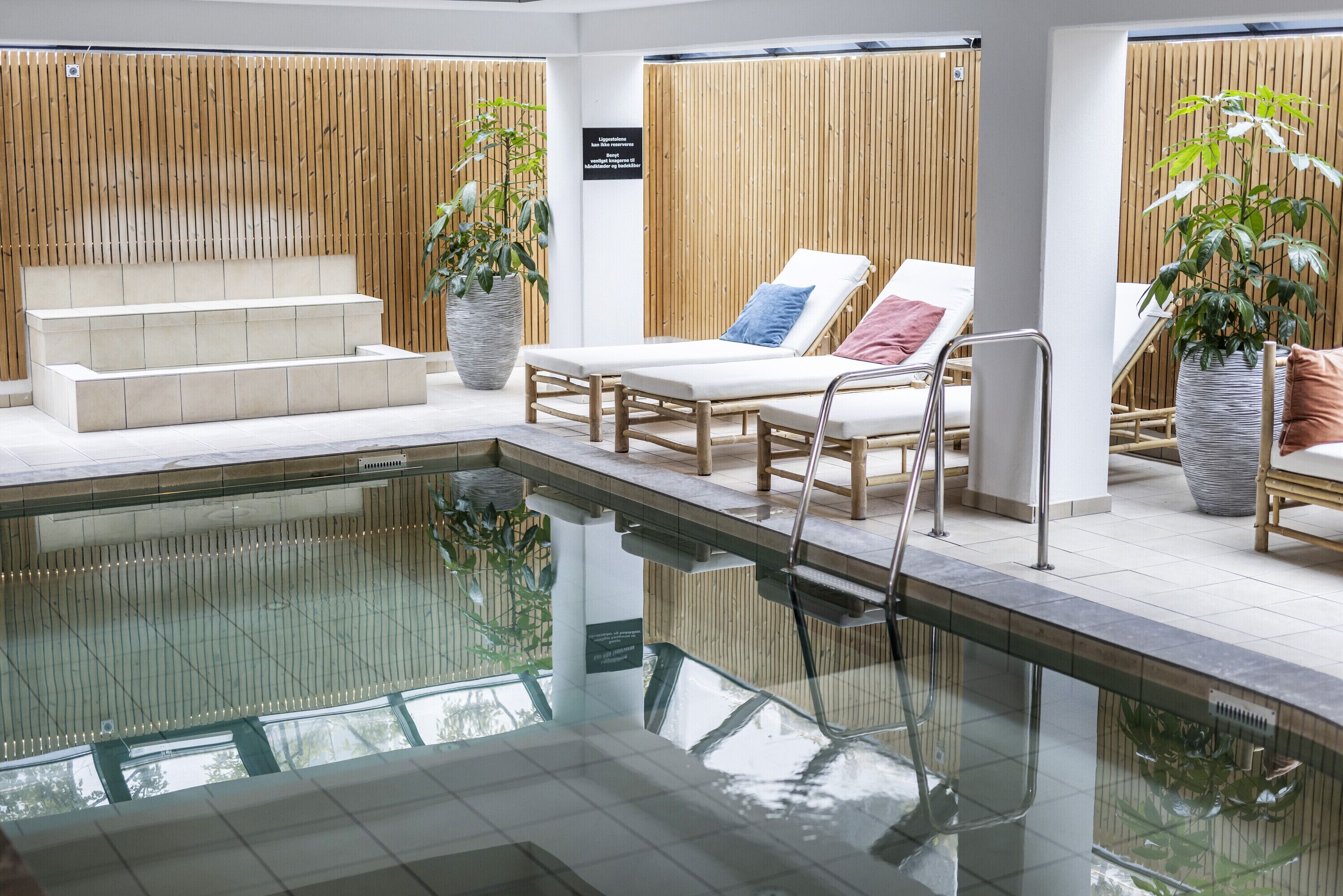 Ein moderner Poolbereich im Innenbereich mit klarem Pool, Liegestühlen und einer Treppe zu höher gelegenen Ebenen.