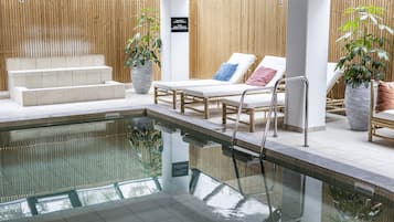 Ein moderner Poolbereich im Innenbereich mit klarem Pool, Liegestühlen und einer Treppe zu höher gelegenen Ebenen.