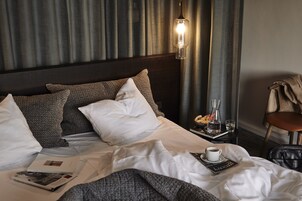 Una cama bien hecha con almohadas blancas y estampadas, una mesita de noche con un vaso de agua, una taza y un libro.