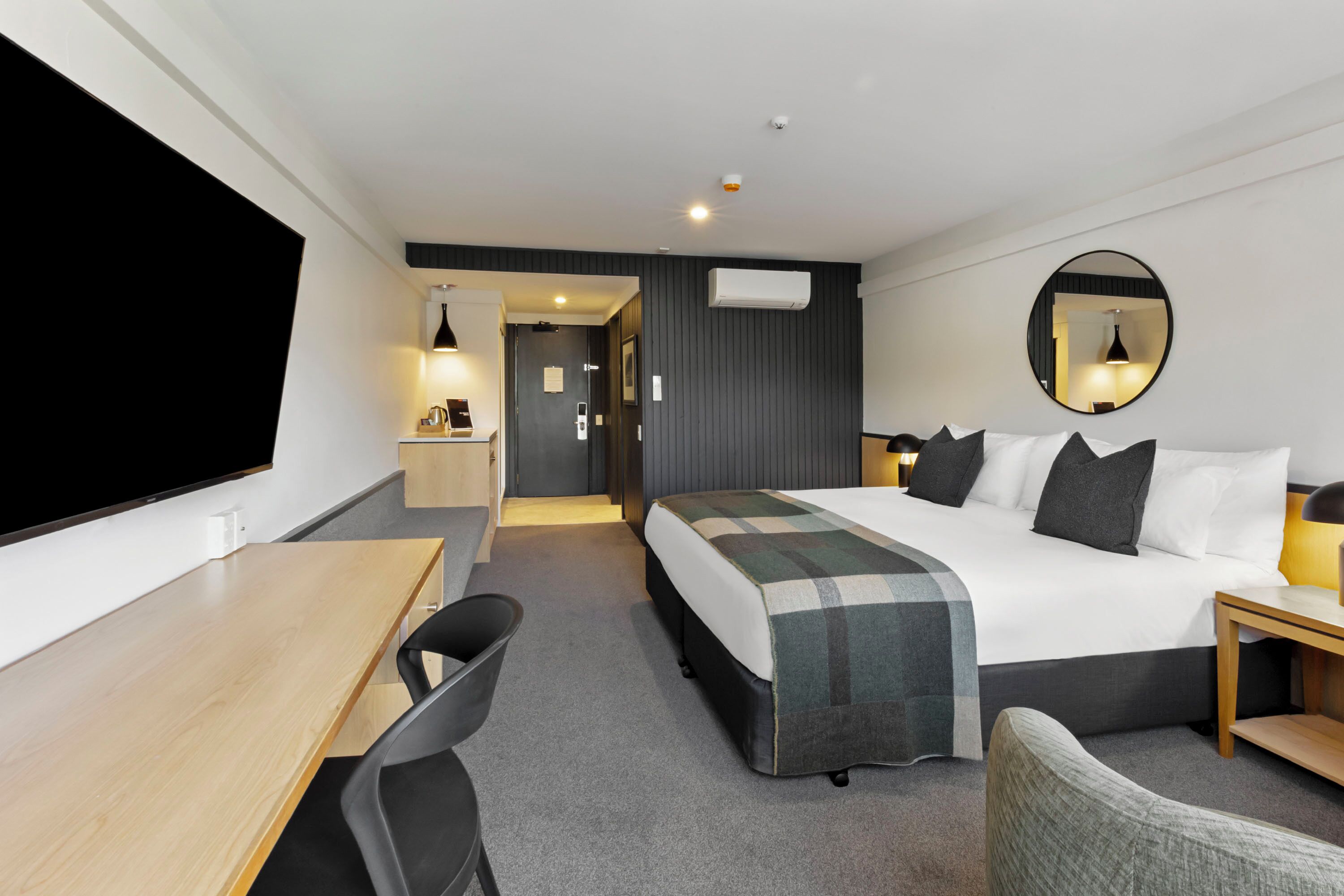 A hotel room with a bed, desk, chair, and a television.