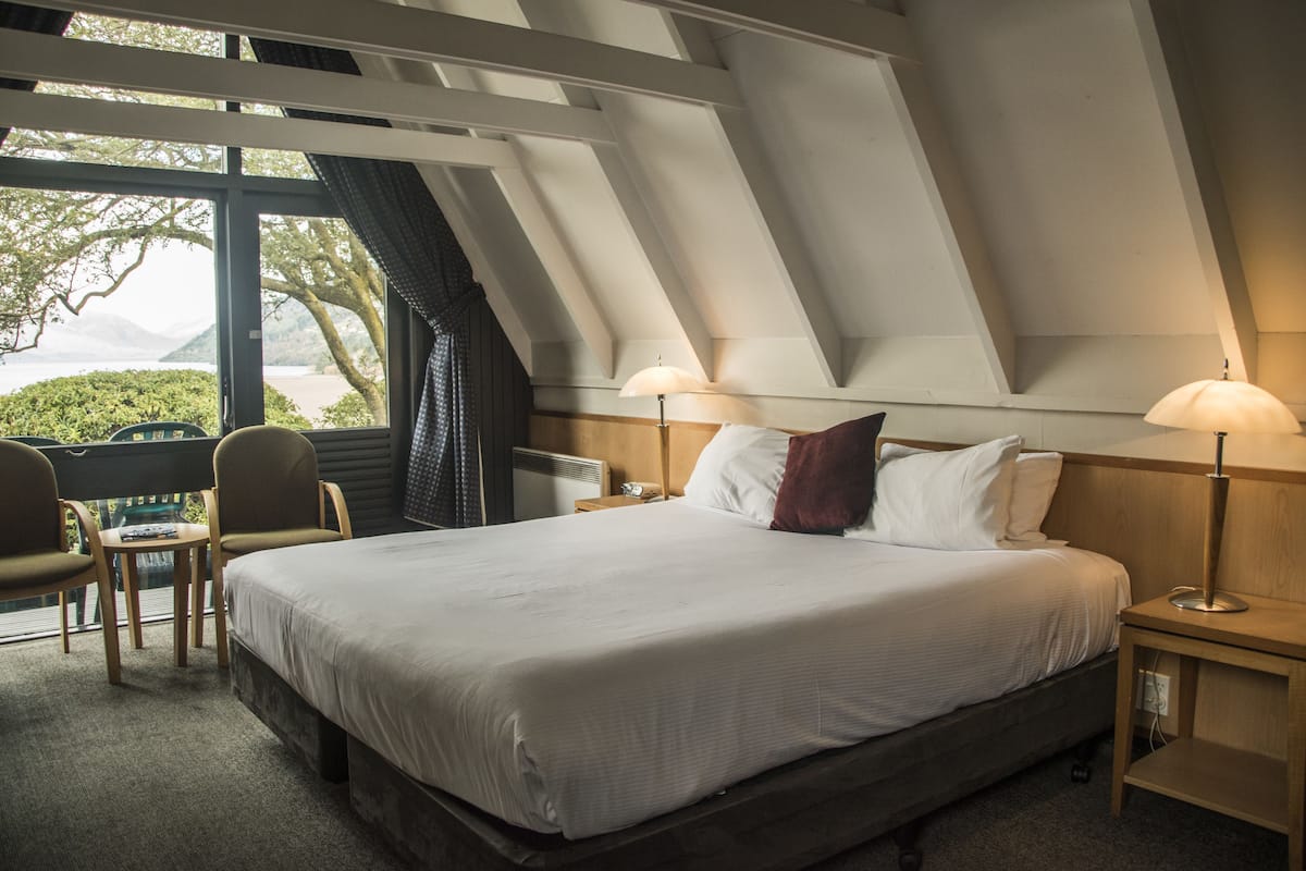 A bedroom with a large bed, two bedside tables, a chair, and a view of the outdoors.