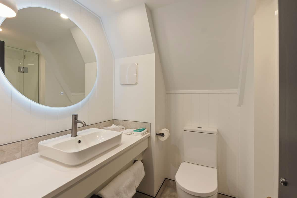 A modern bathroom with a white sink, mirror, and toilet.