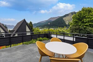 A balcony with wicker chairs and a table, overlooking a mountainous landscape with a lake and buildings in the distance. - Heartland Hotel Queenstown (Queenstown)