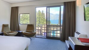 Une chambre d’hôtel comprenant un lit, deux fauteuils, un bureau, une télévision et un balcon avec vue sur la mer et les montagnes.