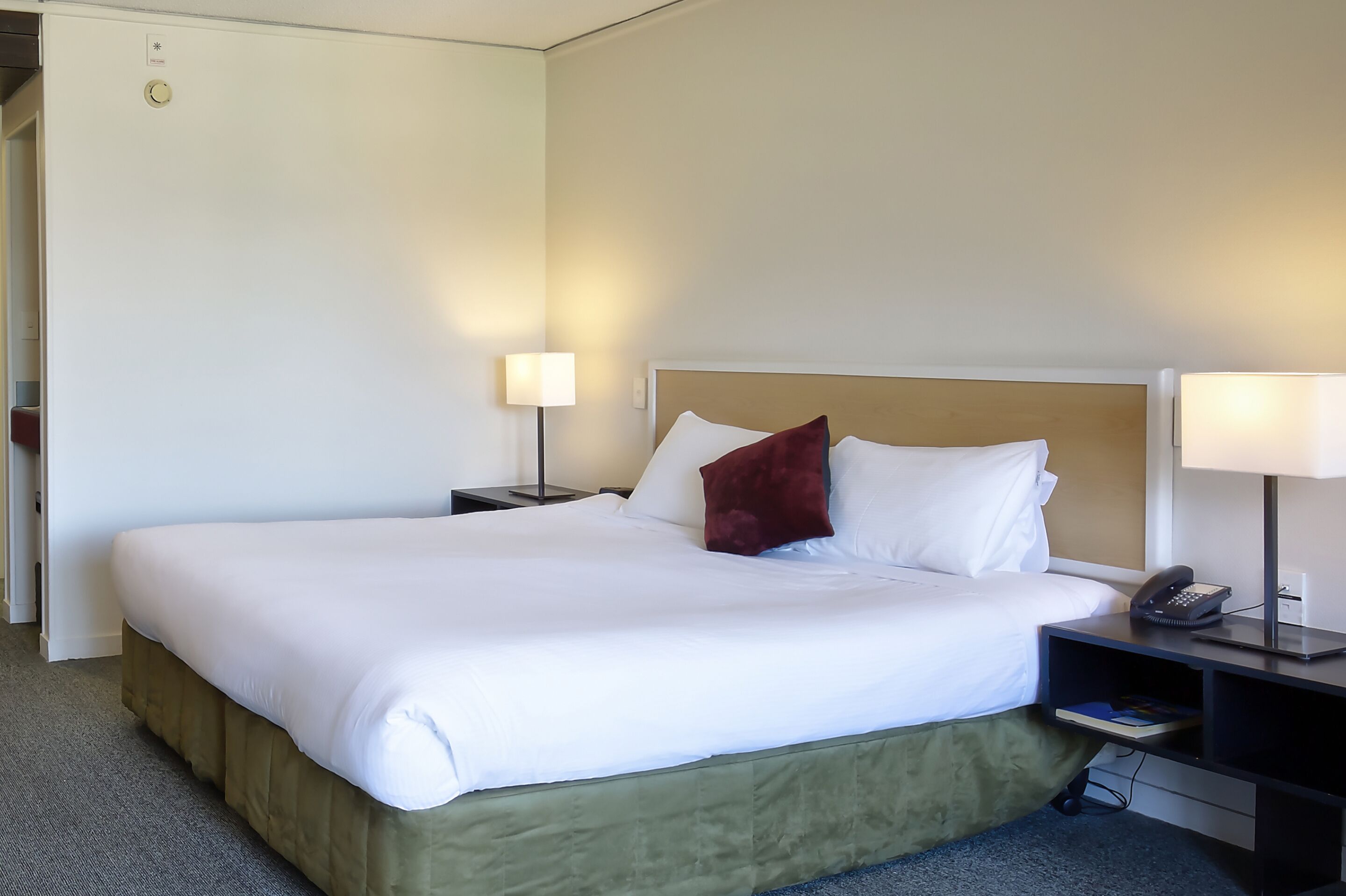 Una habitación de hotel con una cama grande, dos mesitas de noche con lámparas y un cajón pequeño.
