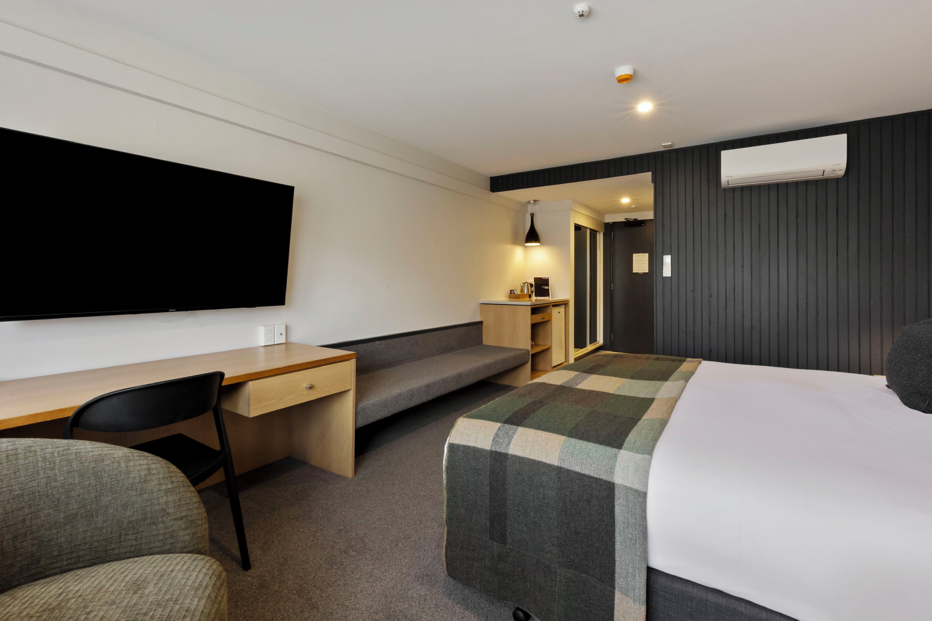 A modern hotel room with a bed, a desk, a chair, a sofa, and a television.