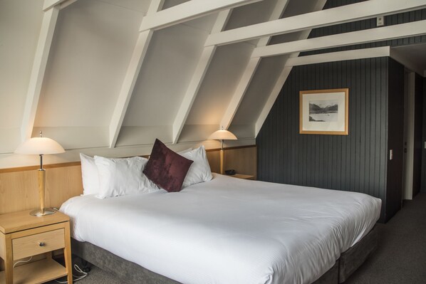Habitación de hotel moderna con una cama grande, dos lámparas de noche, una mesita de noche de madera, una pared de acento oscura y un cuadro enmarcado.