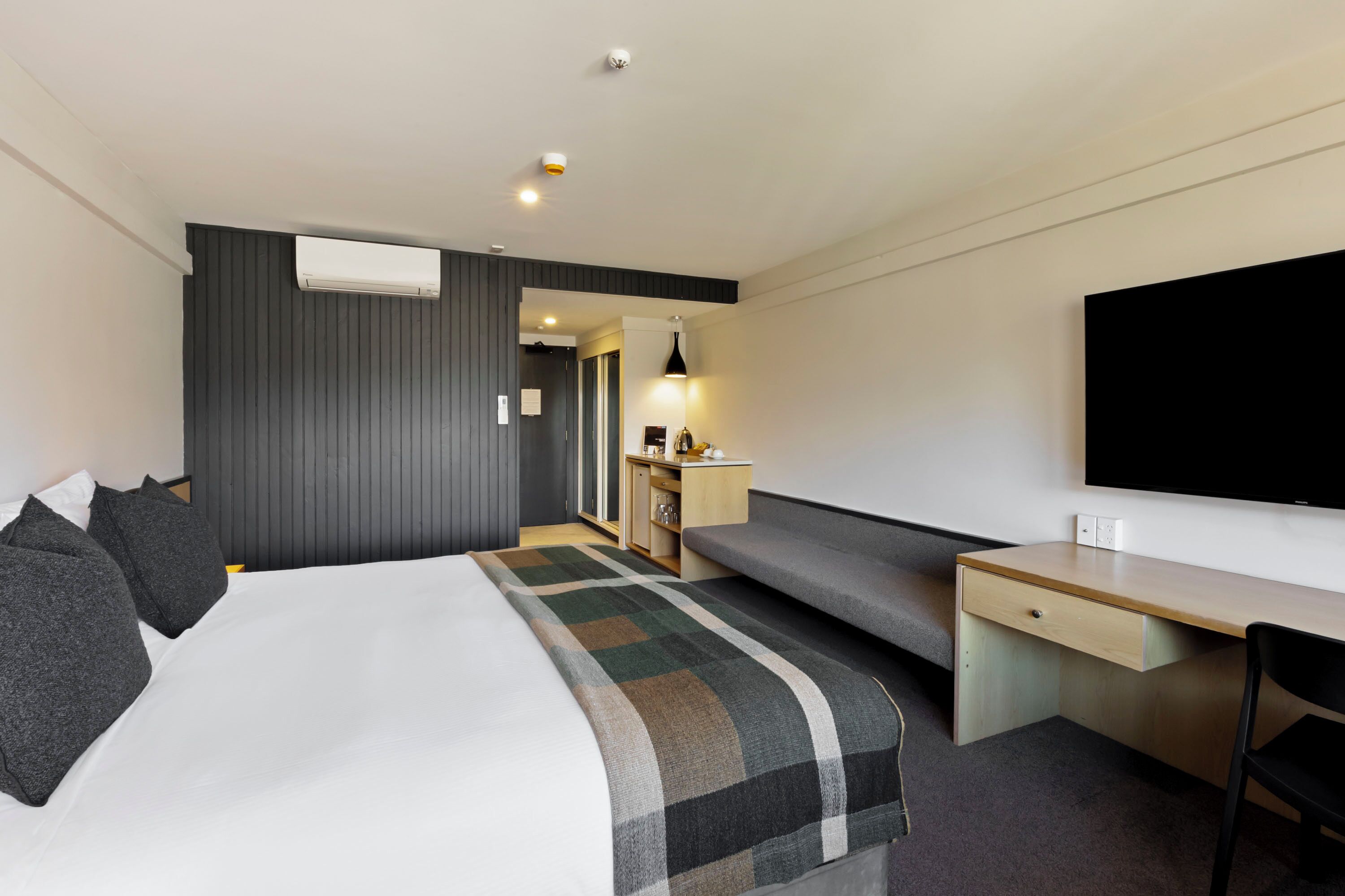 Moderni hotellihuone, jossa on sänky, työpöytä, televisio ja oleskelualue.