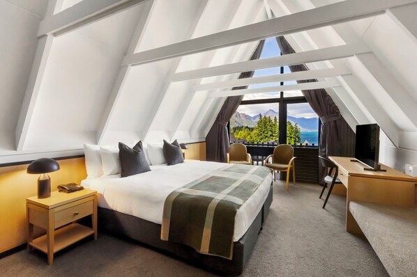 A modern hotel room with a large bed, a desk, and a view of mountains and a lake. - Heartland Hotel Queenstown (Queenstown)