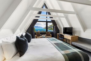 A modern, triangular room with a bed, a desk, a TV, and a view of a lake and mountains. - Heartland Hotel Queenstown (Queenstown)