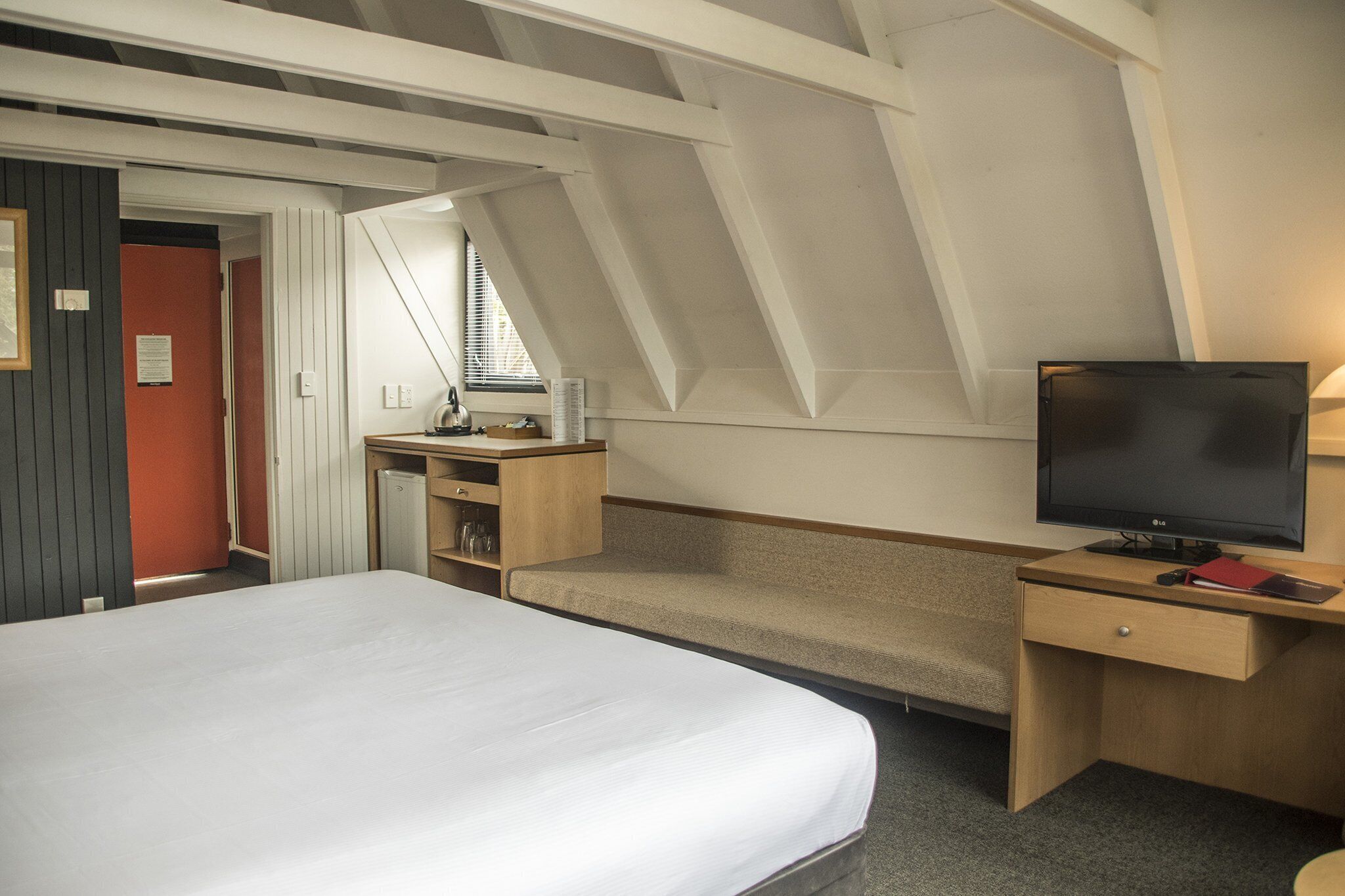 Ein Schlafzimmer mit Bett, Schreibtisch, Fernseher und einem Fenster mit Jalousien.