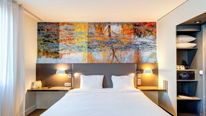 A hotel room with a large bed, two bedside tables with lamps, a nightstand, and a built-in wardrobe with shelves. - B&B HOME Rueil-Malmaison Gare (Rueil-Malmaison)