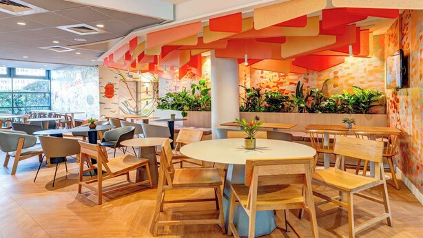 A modern restaurant interior with wooden furniture, a central round table, and vibrant wall art. - B&B HOME Rueil-Malmaison Gare (Rueil-Malmaison)