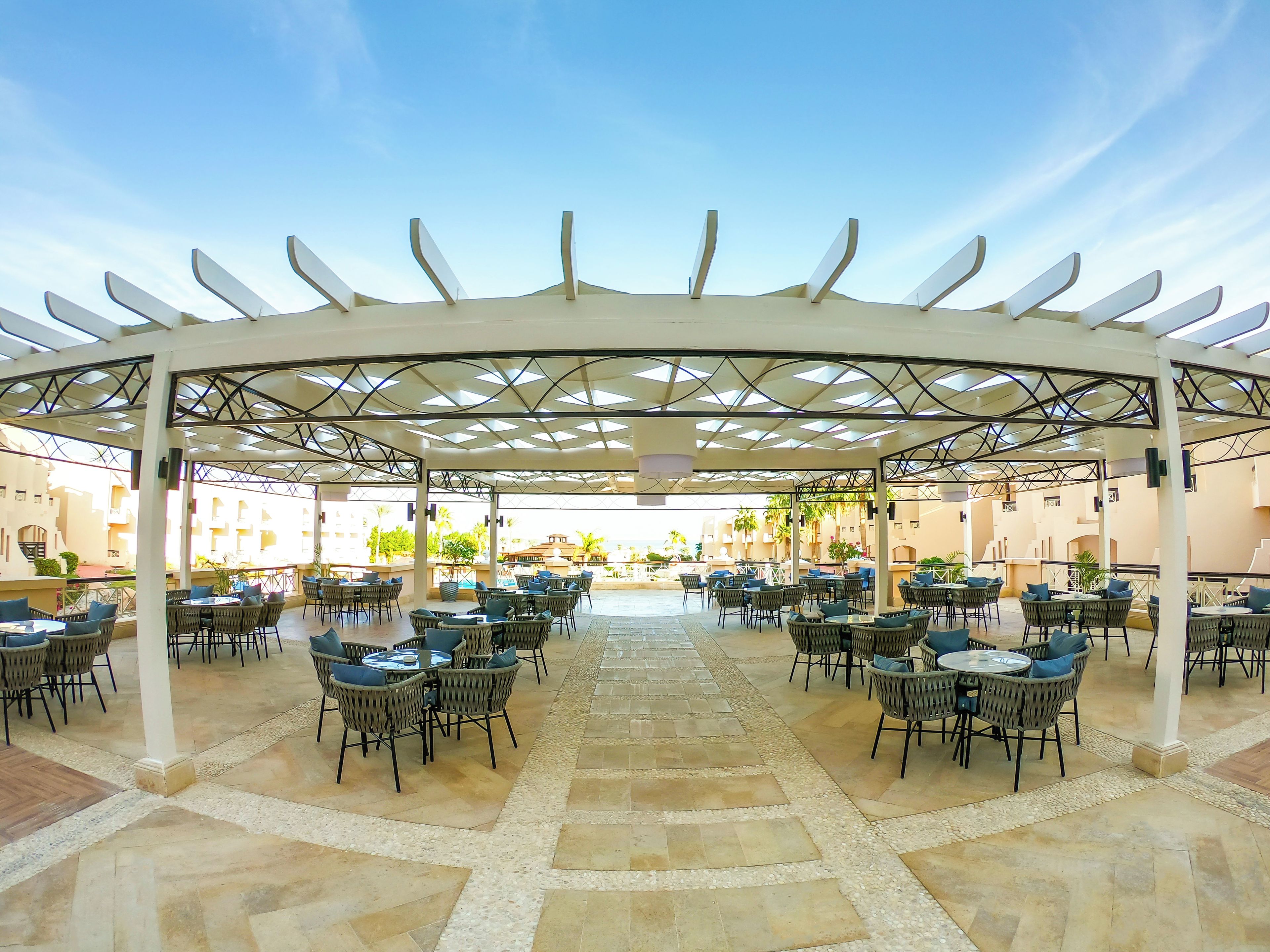 An outdoor dining area with a covered patio, multiple tables and chairs, and a view of buildings in the background.